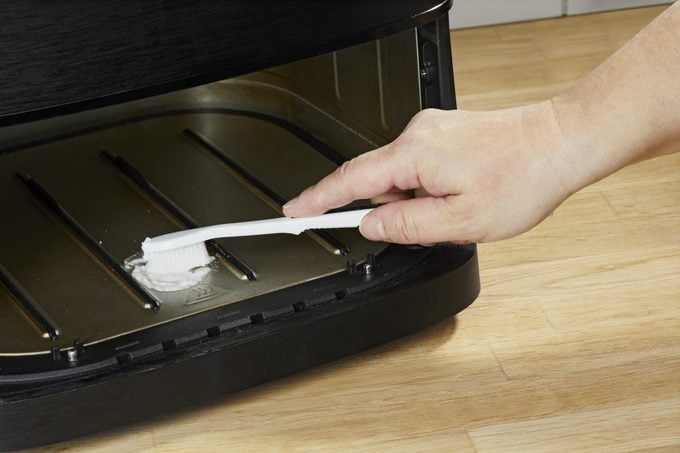 hand appying baking soda paste with a toothbrush to clean buildup inside an air fryer