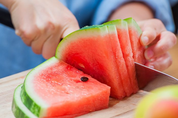 woman cutting watermelon into pieces on a wooden board
