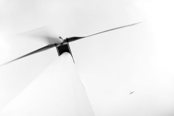 View from below of large electric environmentally friendly wind turbine with aeroplane flying high in the sky - unusual angle