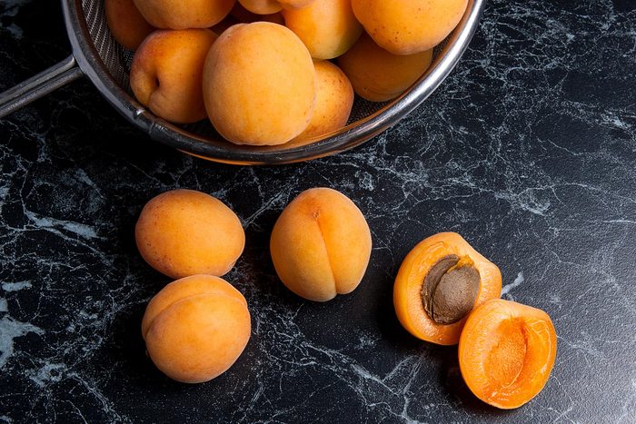 Ripe organic apricots in steel colander. Composition in rustic style - organic yellow juicy apricots in steel colander and whole and halved apricots on dark marble background. Harvest time.