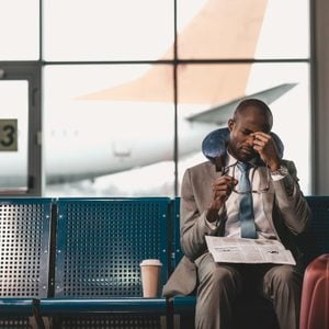 sleepy businessman with travel pillow and newspaper waiting for flight at airport lobby