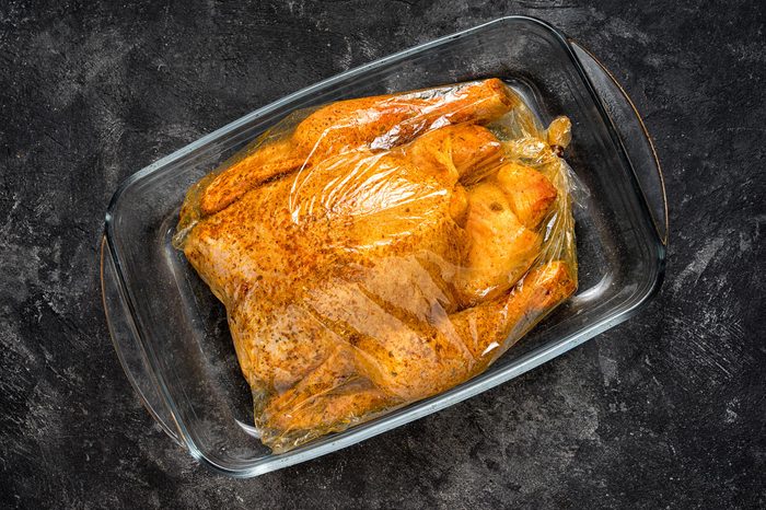 raw whole chicken with spices in a baking bag on a glass tray, ready for cooking on a black cement background.