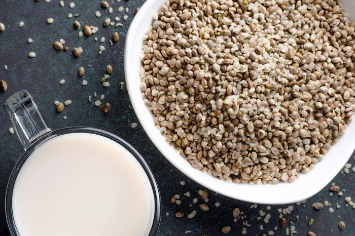 Hemp seed milk in a glass pitcher with hemp seed in a bowl on a dark stone table. Horizontal image, top view, copy space