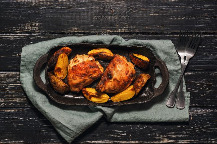 Chicken thigh baked with potatoes on a black dish. Rural background, top view