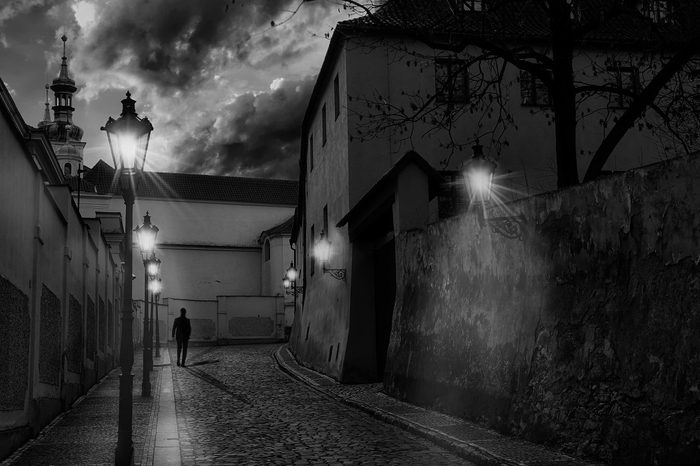 Alley of Prague (located in the Nový Svět area, part of the Hradčany district) with a silhouette of a man walking and several street lights on.