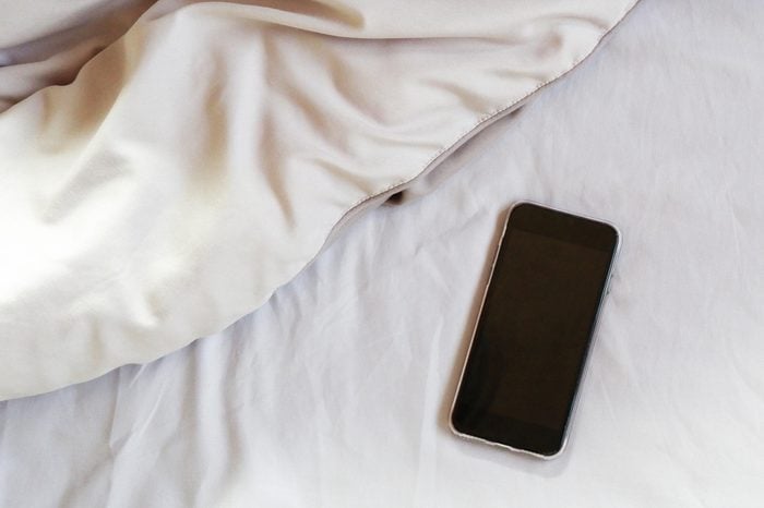 Top view of black smart phone on crease of an unmade bed sheet in the bedroom