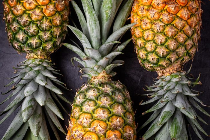 Close up of three ripe fresh pineapples on dark background , top view