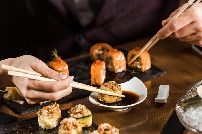 Cropped view of people eating sushi with chopsticks in restaurant
