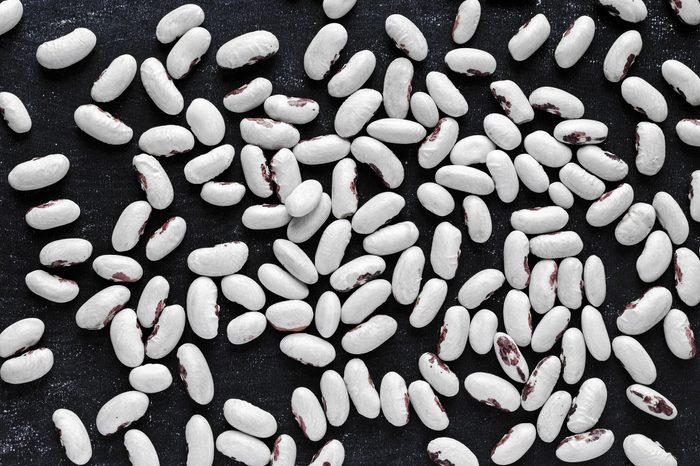 Dry white common beans with red blotches evenly spread on dark blue background. Full frame shot from above