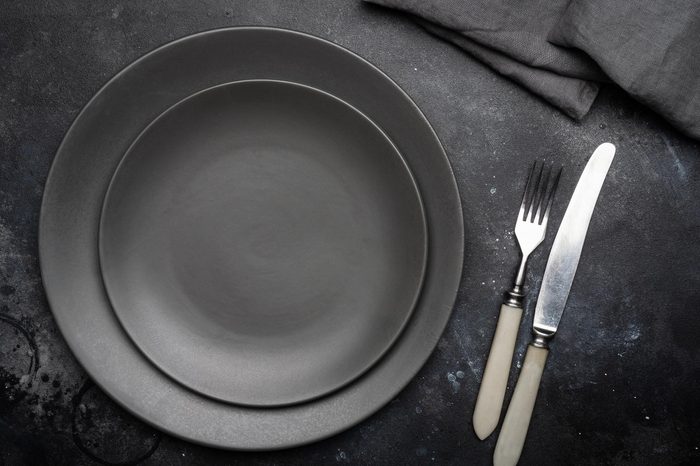 Empty gray plate (ceramic) on a dark gray background with a knife and fork, decorated with a bouquet of lavender and a napkin. Gray minimalistic concept. Copy space.