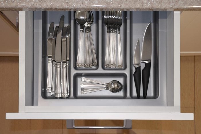 Opened kitchen drawer with a tray and cutlery set with spoons, knife and fork inside. View from above. Image