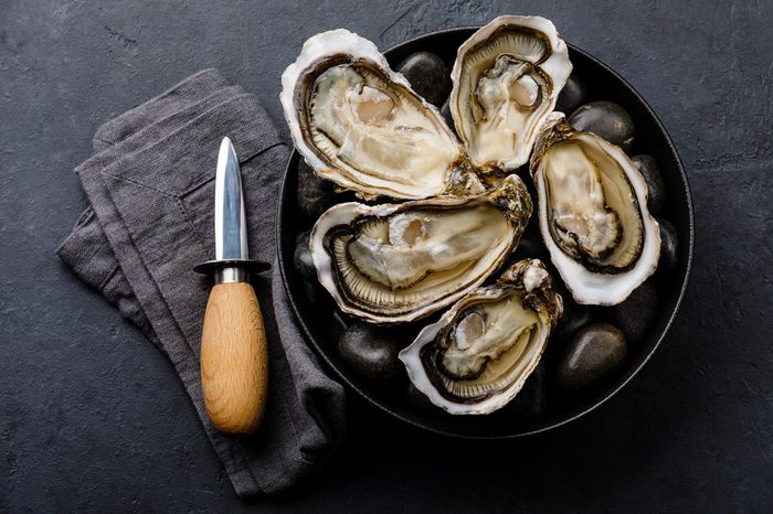 Fresh Oysters with lemon and knife on stones on dark background
