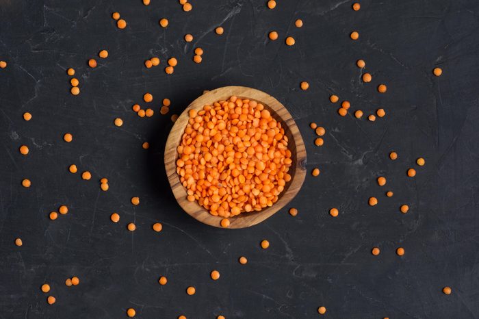 Red lentils in wooden bowl on a dark concrete background. Top view or flat lay