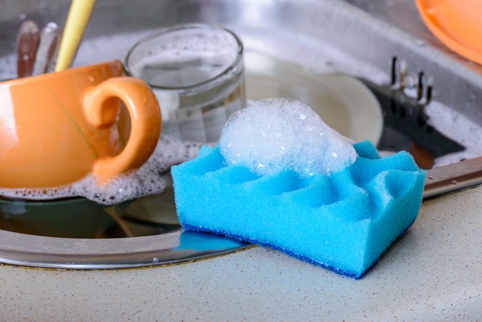 Cleaning the dirty dishes with a blue sponge with detergent in a sink