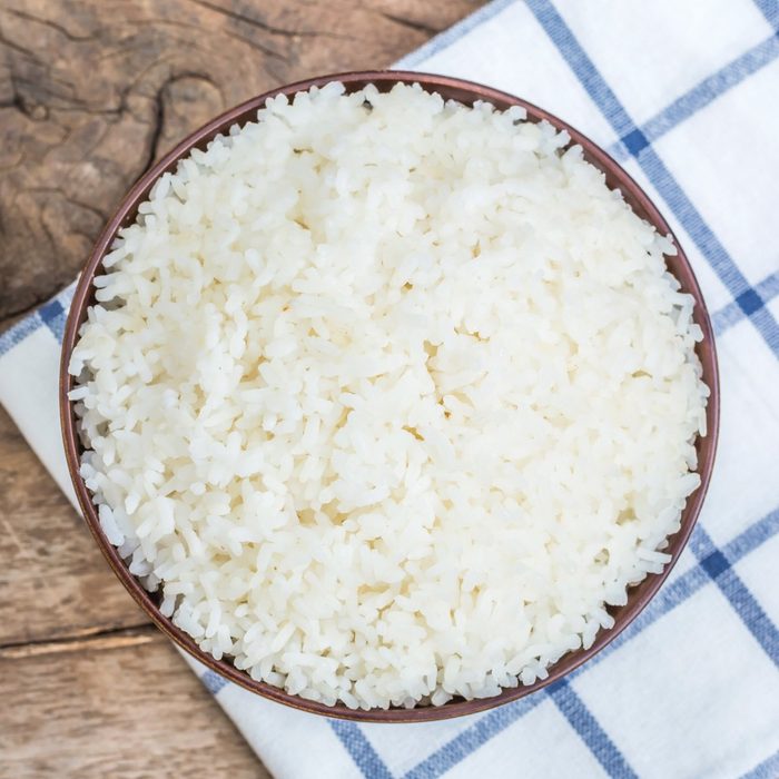 Cooked rice in bowl with spoon and dishcloth