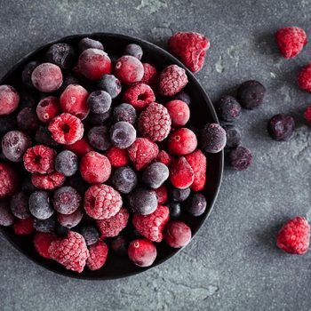 Frozen raspberry, blueberry, cranberry on black background. Frozen fruit. Top view, flat lay, close up.
