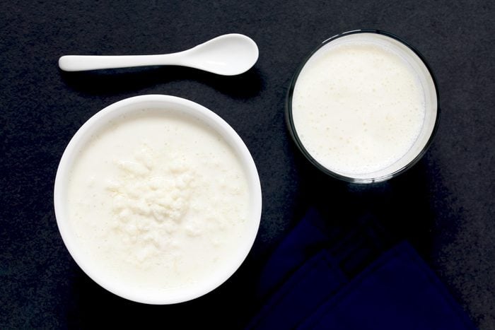 Kefir grains in milk with a glass of fresh kefir drink on the side, photographed overhead on slate with natural light (Selective Focus, Focus on the top of the kefir grains and the kefir drink)
