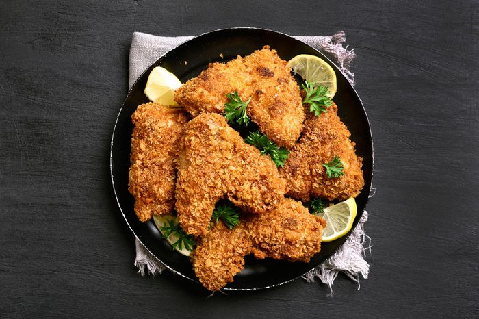 Fried breaded chicken wings on plate over black background.