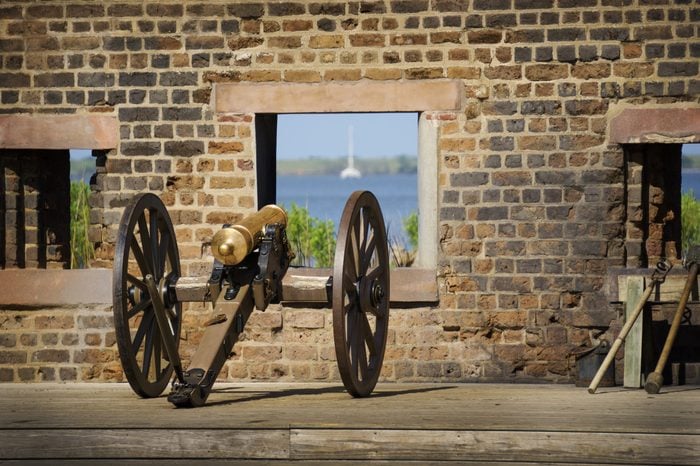 A horizontal view of an antique cannon overlooking the ocean through a window on a brown brick wall at Fort James Jackson in Savannah,Georgia.