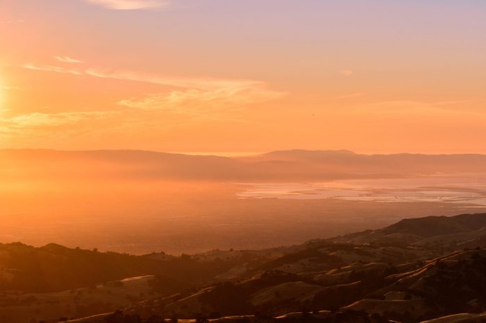 Sunset views of the south San Francisco bay area and the surrounding hills as seen from the top of Mt Hamilton; a thin layer of fog creates a soft orange colored light; San Jose, California