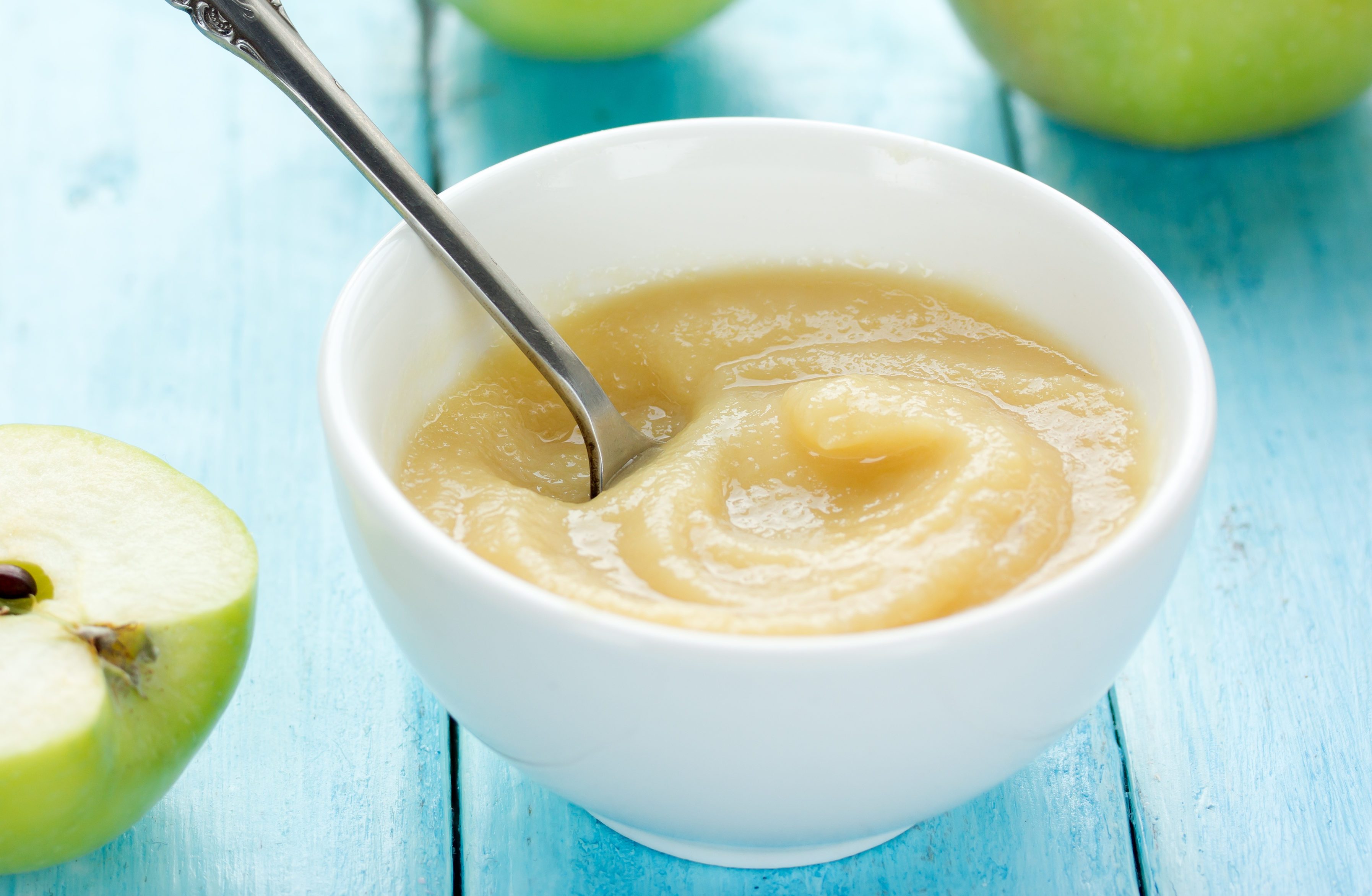 Healthy organic applesauce (apple puree, mousse, baby food, sauce) in white bowl on table with green apples