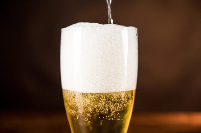 Golden cold beer being poured into the glass with frothy foam