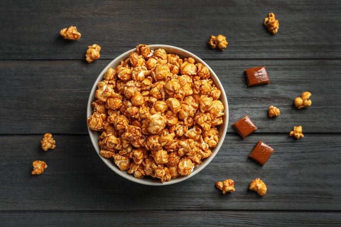 Delicious popcorn with caramel in bowl and candies on wooden background, top view