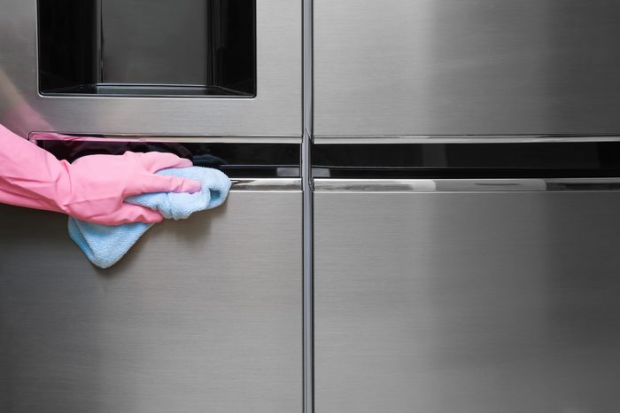 Employee hand in rubber protective glove with micro fiber cloth wiping a fridge's stainless doors. Early spring or regular cleanup. Commercial cleaning company concept.