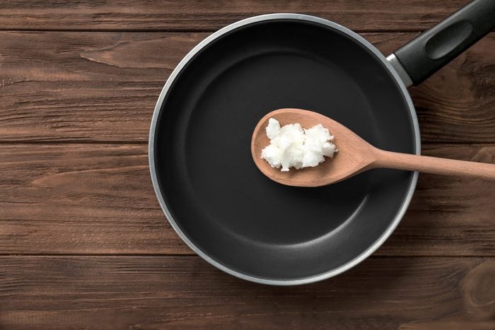 Wooden spoon with coconut oil in frying pan on table