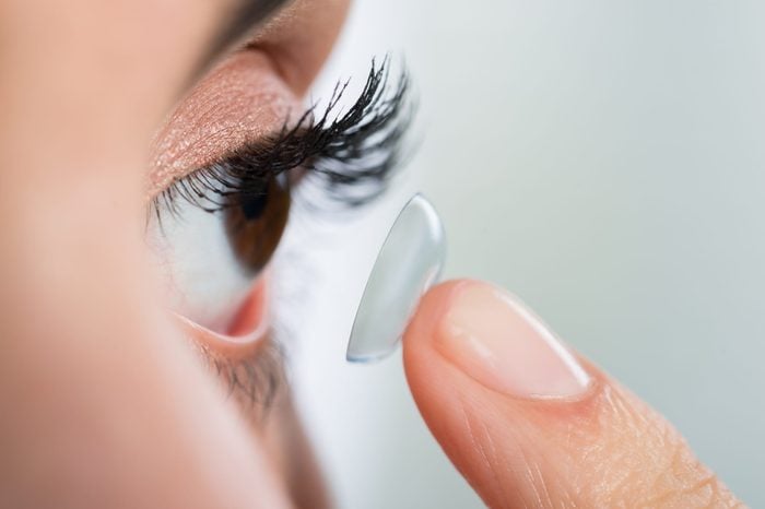 Closeup of young woman wearing contact lens at home
