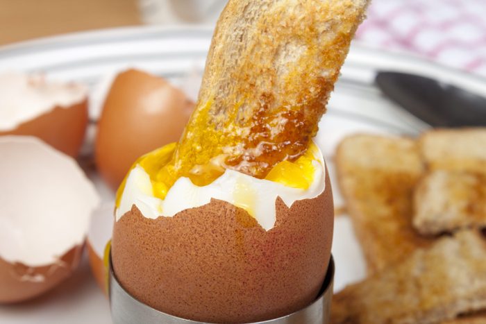 Close up shot of a golden toasted bread soldier dipped in a runny egg on a plate