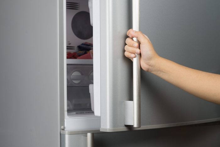 Hand of a woman is opening a refrigerator door