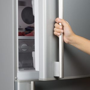 Hand of a woman is opening a refrigerator door