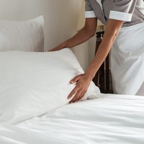 anonymous housekeeping worker making up a bed in a hotel room