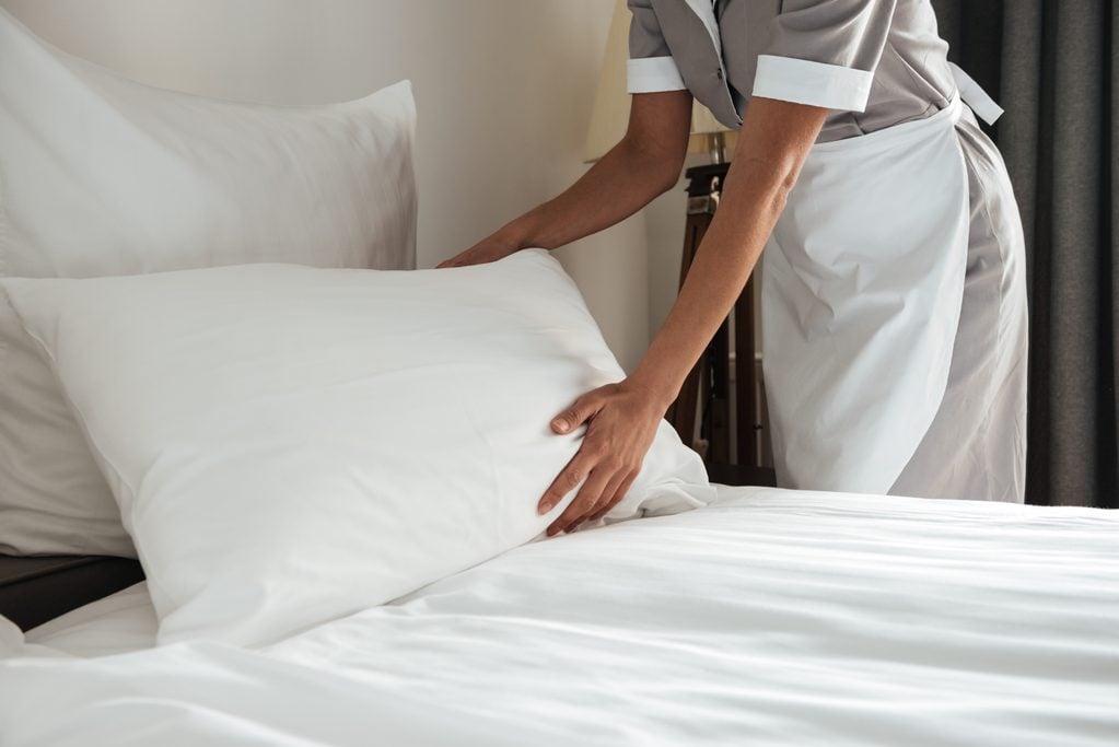 anonymous housekeeping worker making up a bed in a hotel room