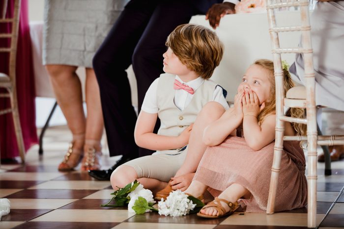Children are sitting on the dancefloor by a table at a wedding. They are watching the bride and groom share their first dance. 