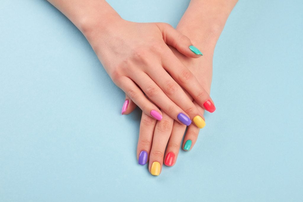 Female beautiful manicured hands. Woman hands with stylish colorful nails on light blue background. Skin and nail care.