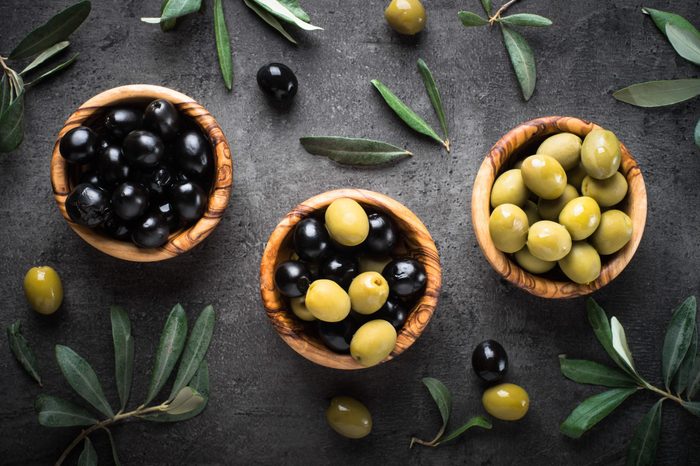 Black and green olives in wooden bowls. Top view on black background.