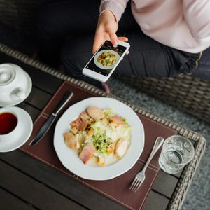 Girl hand holding smartphone and taking photo of food on wooden table. Top view.