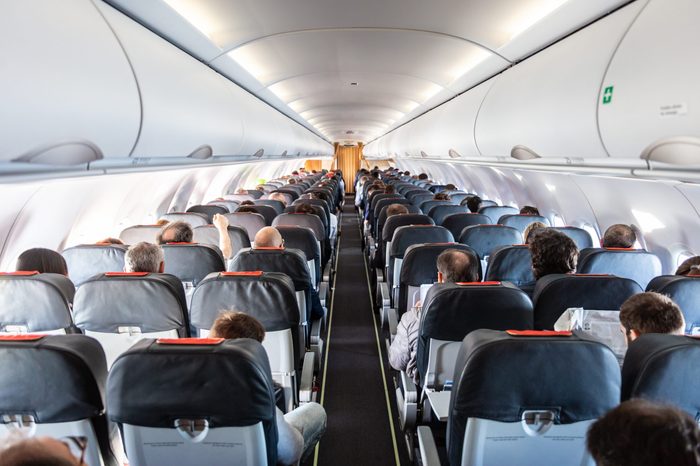 Interior of commercial airplane with unrecognizable passengers on their seats during flight shot from the rear of airplane.
