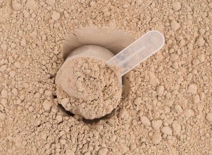 Top close of ground chocolate flavored plant protein with a plastic measuring scoop.
