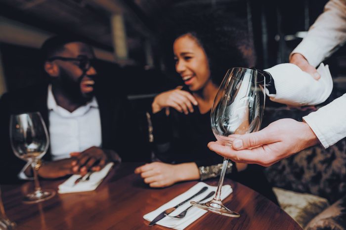 Waiter Pouring Wine to Glass Couple in Restaurant. Romantic African American Couple in Love Dating. Cheerful Man and Woman Drinking Red Wine. Romantic Concept. Anniversary. Bottle of Red Wine.