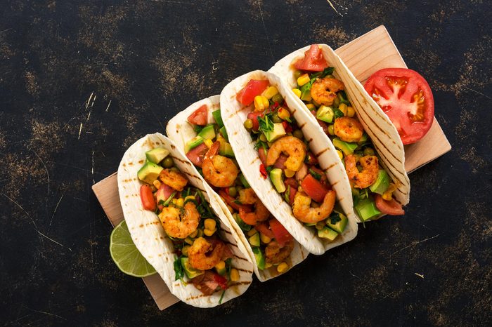 Shrimps tacos with salsa, vegetables and avocado on a dark background. Mexican food.Top view
