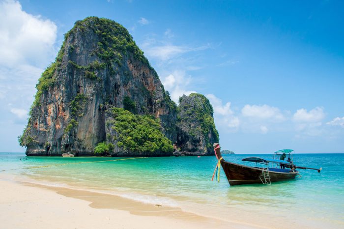 Nice beach and turquoise water with the limestone island and a small boat besides at Krabi Thailand