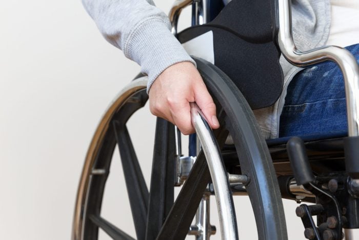 Detail of disabled woman holding a hand on wheel of a wheelchair. Close up.