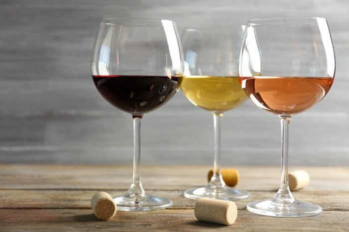 Wine glasses in a row and corks on wooden table against grey background