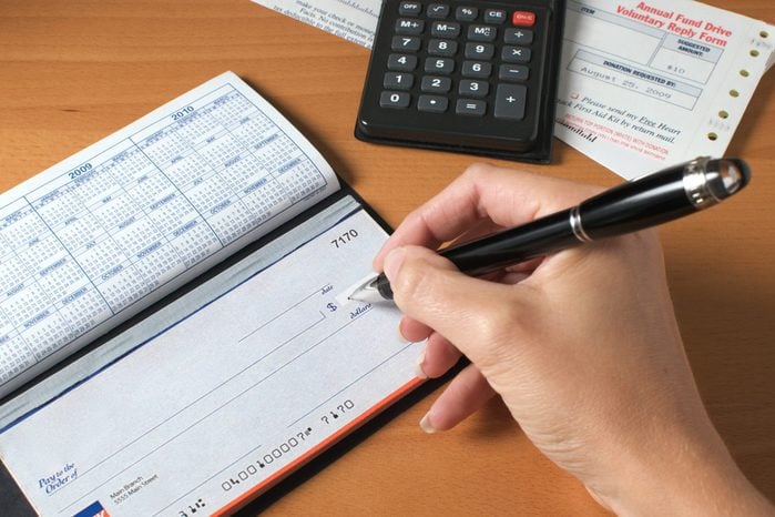 Woman's hand writing a check to pay the bills, with calculator and an invoice on the desktop.