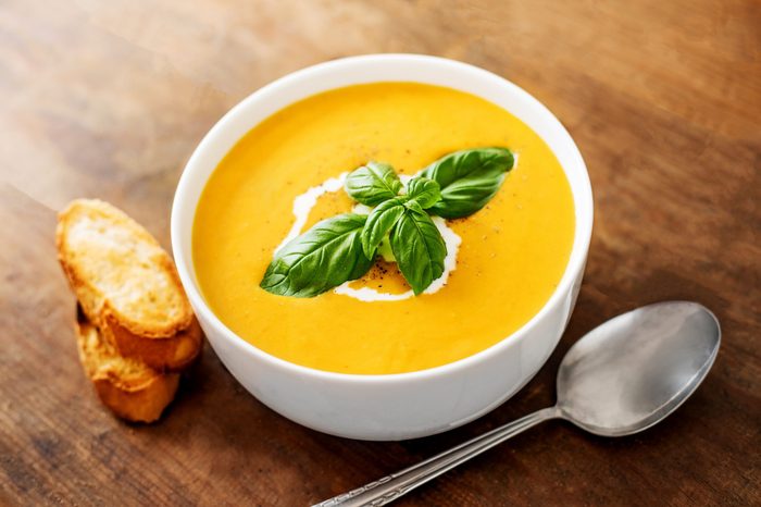 Bowl of squash soup with basil leaf on wood table. Pumpkin soup served in a bowl, top view