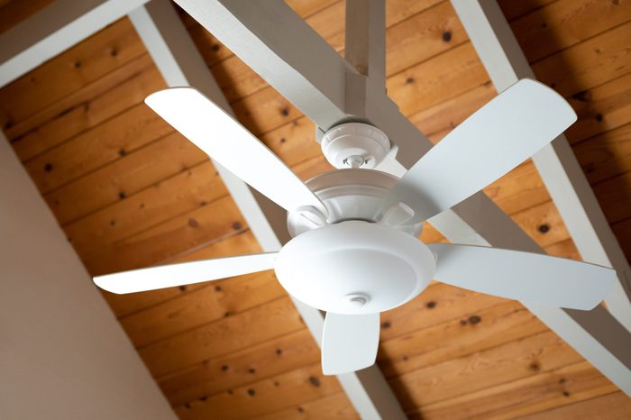 Close up on a white ceiling fan on an exposed support beam, with a vaulted wood ceiling, in the living room of a modern home, with space for text on the left