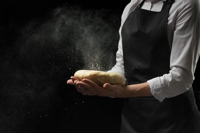 Dough in the hands of the chef's chief with flour on a dark background. The concept of cooking food, pizza, sweets, pastas, bread and bakery products